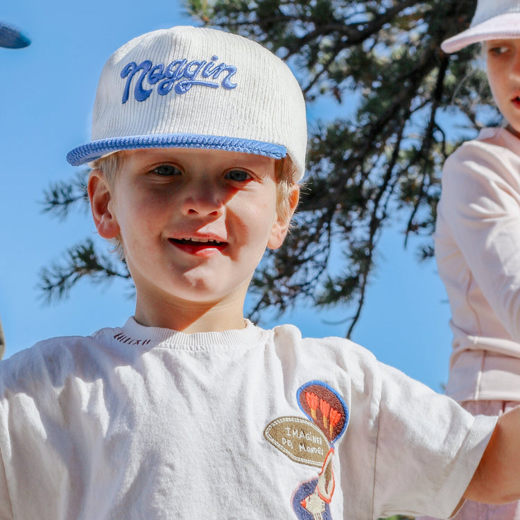 Three children wearing white caps with branding, standing outdoors against a blue sky.