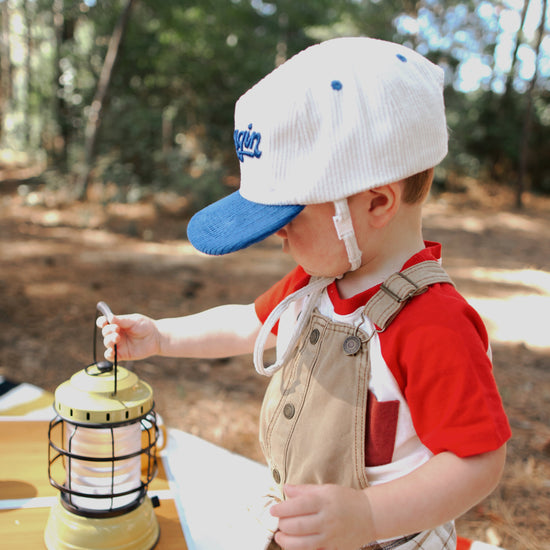 Child in a camping outfit with a lantern and mug outdoors