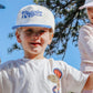 Three children wearing white caps with branding, standing outdoors against a blue sky.