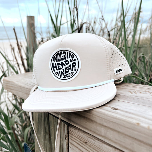 White sandal with a black logo on a wooden surface with plants in the background
