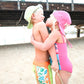 Two children in swimsuits and hats standing on a sandy beach with a wooden pier in the background.