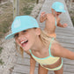Two children wearing light blue caps and swimwear on a wooden boardwalk.